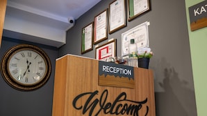 A reception desk with a 'Welcome' sign, a clock, and framed certificates on the wall.