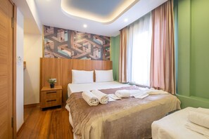 A hotel room with a large bed, a wooden nightstand with a plant, a geometric-patterned wall, and a window with curtains.
