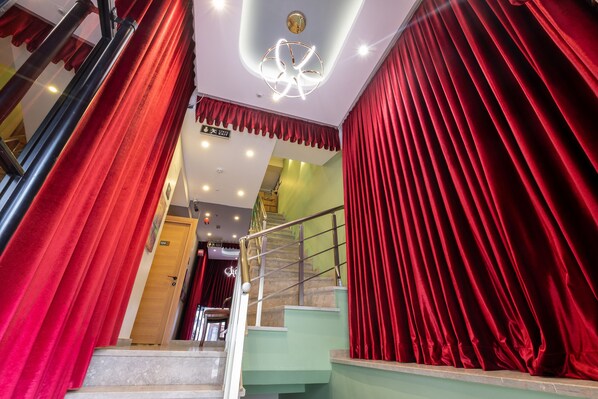 A staircase with red curtains on both sides, a modern light fixture, and a green wall in the background.