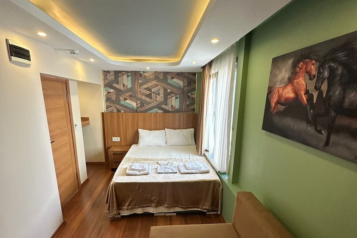 A hotel room with a bed, a sofa, a painting of horses, and a patterned wall.