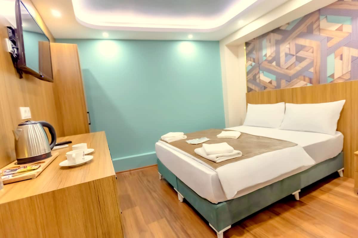 A modern hotel room with a bed, a wooden desk, a kettle, and a wall-mounted TV.