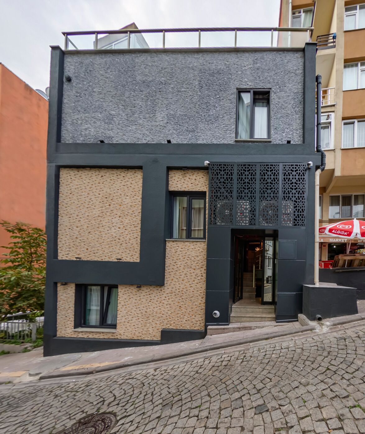 Un bâtiment moderne à deux étages, doté d’une façade noire et beige, d’un mur orné de motifs et d’une fenêtre décorative à croisillons.