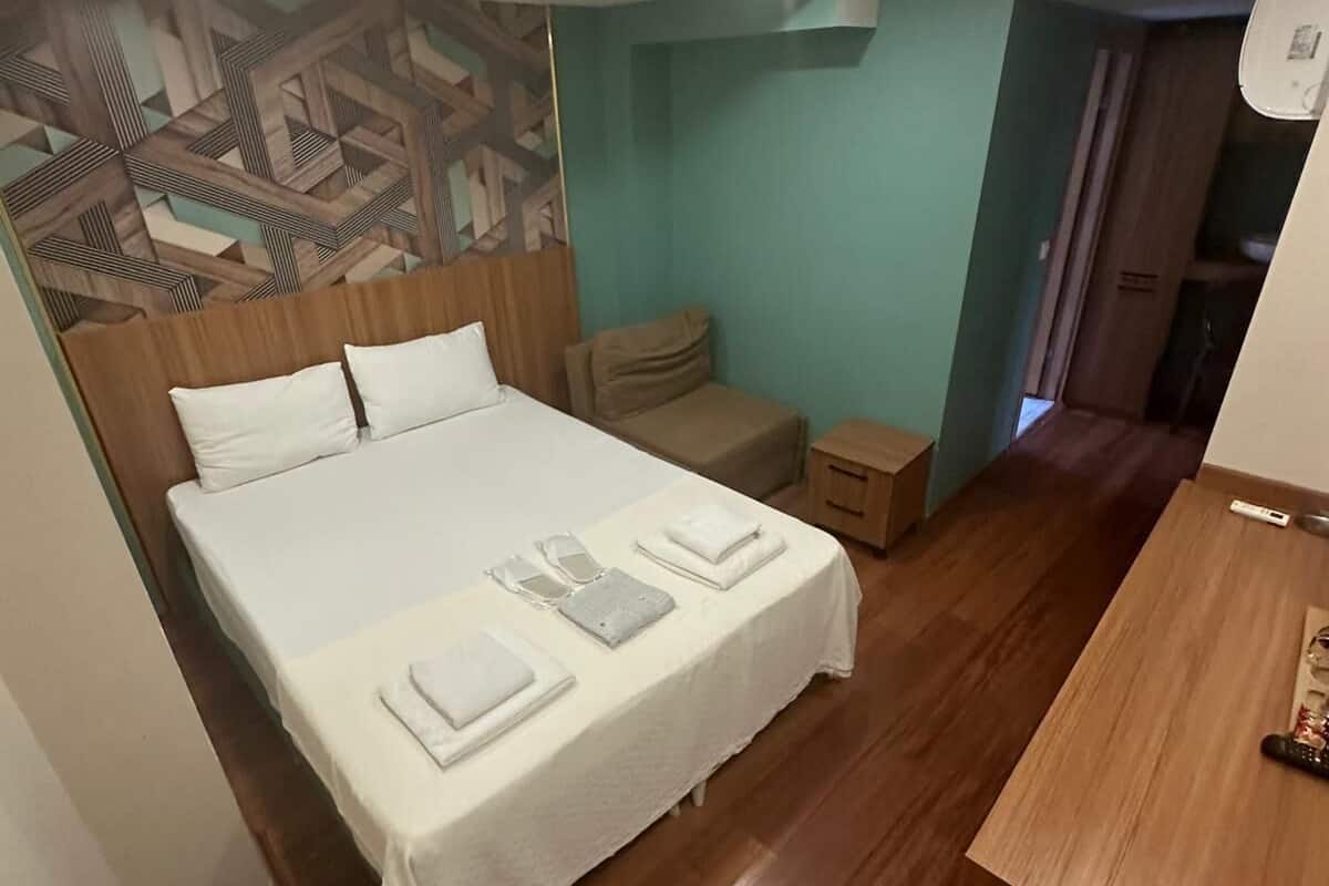 A hotel room with a bed, bedside table, and a small wooden nightstand.