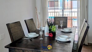 Mesa de comedor preparada con platos, cuencos y copas blancos, un jarrón con flores y una botella de champán.