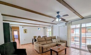 Un salón con sofá, una mesa de centro, ventilador de techo y vistas amplias por las ventanas.