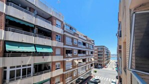 Un edificio residencial de varios pisos con balcones, vista a la calle y automóviles estacionados.