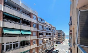 A multi-story residential building with balconies, a street view, and parked cars.