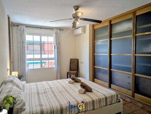 A hotel room with a bed, a ceiling fan, a window with curtains, a wall-mounted air conditioner, and a sliding glass door. - 3BR Family Apt Near Beach  AC TV17 (Torrevieja)