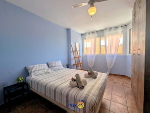 Un dormitorio con cama, ventilador de techo, ventana con cortinas y armario de madera.