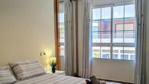 Habitación de hotel con cama, lámpara de noche, ventana con cortinas y vista a un edificio.