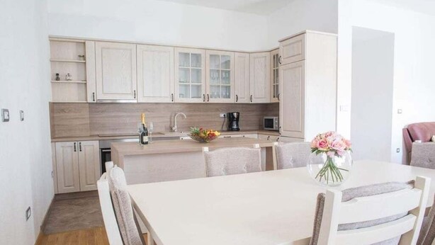 A modern kitchen with light wooden cabinets, a white countertop, and a dining area with a white table and chairs.