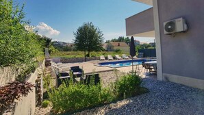 A pool area with lounge chairs and a small table, surrounded by gravel and plants.
