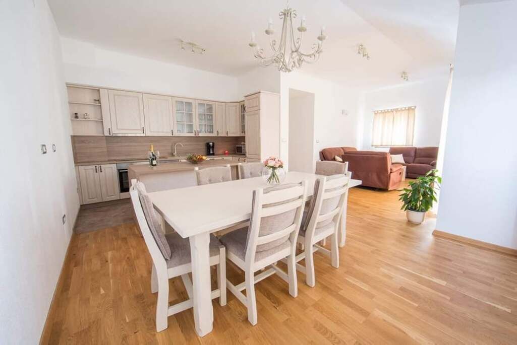 A modern kitchen with white cabinets, a dining table with chairs, and a chandelier.