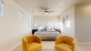 Un dormitorio con una cama, dos sillones amarillos, un ventilador de techo y una ventana.