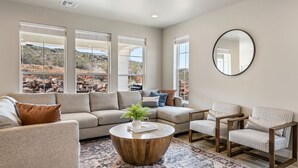 A modern living room with a sectional sofa, two armchairs, a round coffee table, and large windows offering a view of a rocky landscape. - Grand Getaway: Sleeps 20, reunion or corporate (Washington)