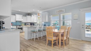 Una cocina moderna con armarios blancos, una isla central y un comedor con sillas de madera.