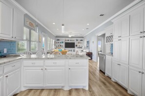 A spacious kitchen with white cabinetry, a central island, and a dining area with chairs.