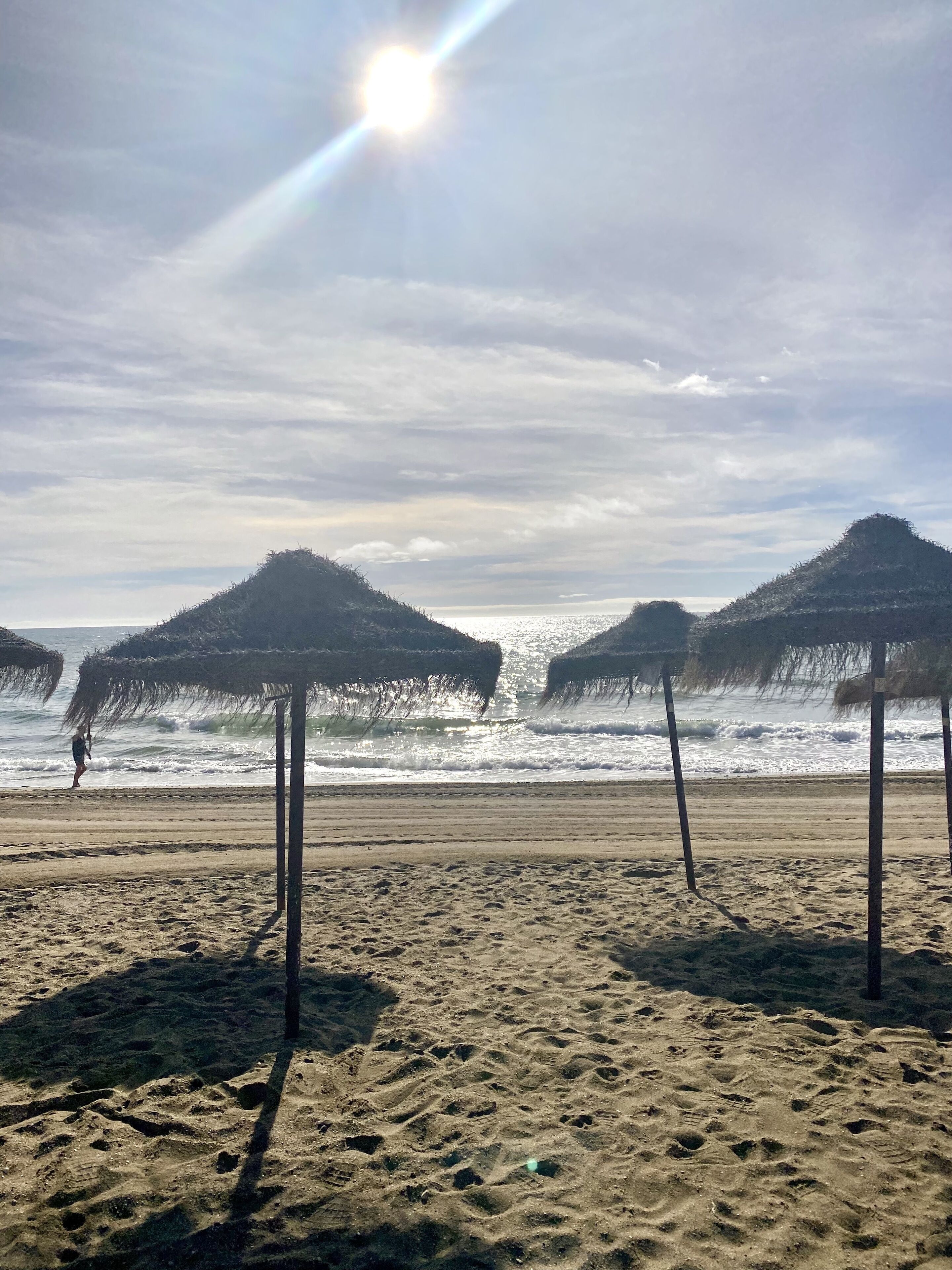A beach with thatched umbrellas and a person walking along the shore.