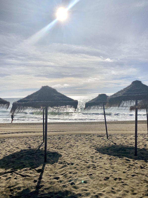 A beach with thatched umbrellas and a person walking along the shore.