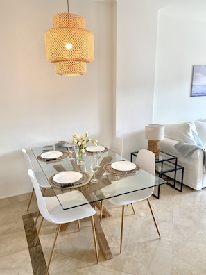 A modern dining area with a glass table, white chairs, and a woven pendant light.