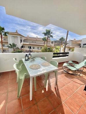 A terrace with a table and chairs, a rocking chair, and a view of buildings and palm trees.