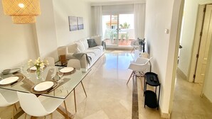 A modern living room with a glass dining table, white sofas, and a balcony with a view. - Beautiful apartment (Mijas)