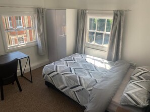 A bedroom with a bed, a desk, and two windows. - Castle Hill Resident (Cambridge)