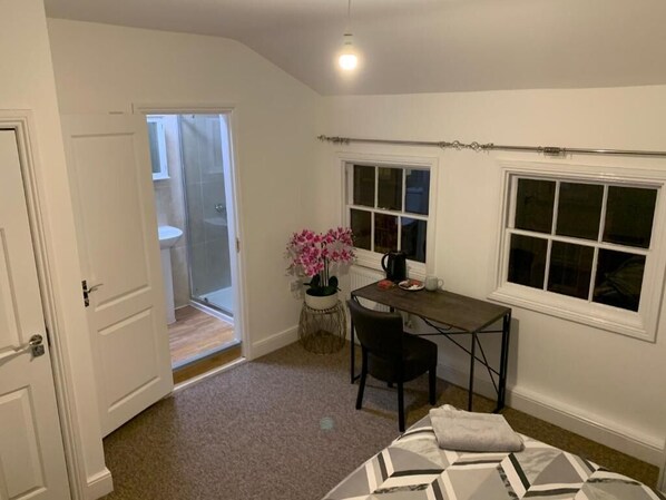 Une chambre à coucher comprenant un lit, un bureau, une chaise, une fenêtre et une porte donnant sur une salle de bain.