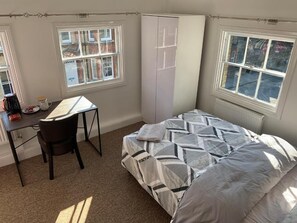 A bedroom with a bed, a desk, and a chair. There are windows on two sides of the room. - Castle Hill Resident (Cambridge)