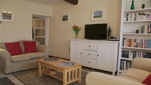 A living room with a sofa, a coffee table, a television, a bookshelf, and a door. - Country Hideaways | Barton Cottage | West Burton (Leyburn)