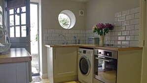 A compact kitchen with a washing machine, oven, and a small window. - Country Hideaways | The Hay Loft | Ripon (Ripon)