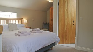 A bedroom with a bed, bedside lamps, a wooden wardrobe, and a door leading to another room. - Country Hideaways | The Hay Loft | Ripon (Ripon)