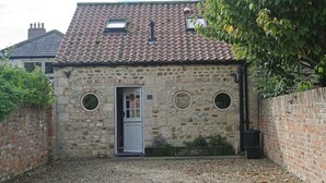 A stone building with a tiled roof, a white door, and three circular windows. - Country Hideaways | The Hay Loft | Ripon (Ripon)