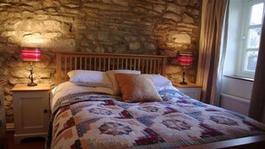 A bed with a quilt, two bedside lamps, a wooden headboard, and a stone wall. - Country Hideaways | The Old Wheelhouse | West Burton (Leyburn)