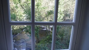 A window with a view of a stream surrounded by greenery. - Country Hideaways | The Old Wheelhouse | West Burton (Leyburn)
