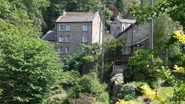 A stone building with multiple windows, surrounded by lush greenery and trees. - Country Hideaways | The Old Wheelhouse | West Burton (Leyburn)