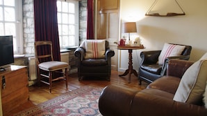 A cozy living room with a fireplace, leather armchairs, a wooden coffee table, and a television on a wooden cabinet. - Country Hideaways | The Old Wheelhouse | West Burton (Leyburn)