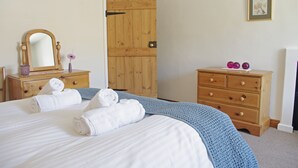 A bedroom with a bed, a wooden wardrobe, a dresser, a mirror, and a door. - Country Hideaways | Jesmond Cottage | West Burton (Leyburn)