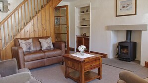 A living room with a brown leather sofa, a wooden coffee table, a fireplace, and a staircase. - Country Hideaways | Jesmond Cottage | West Burton (Leyburn)