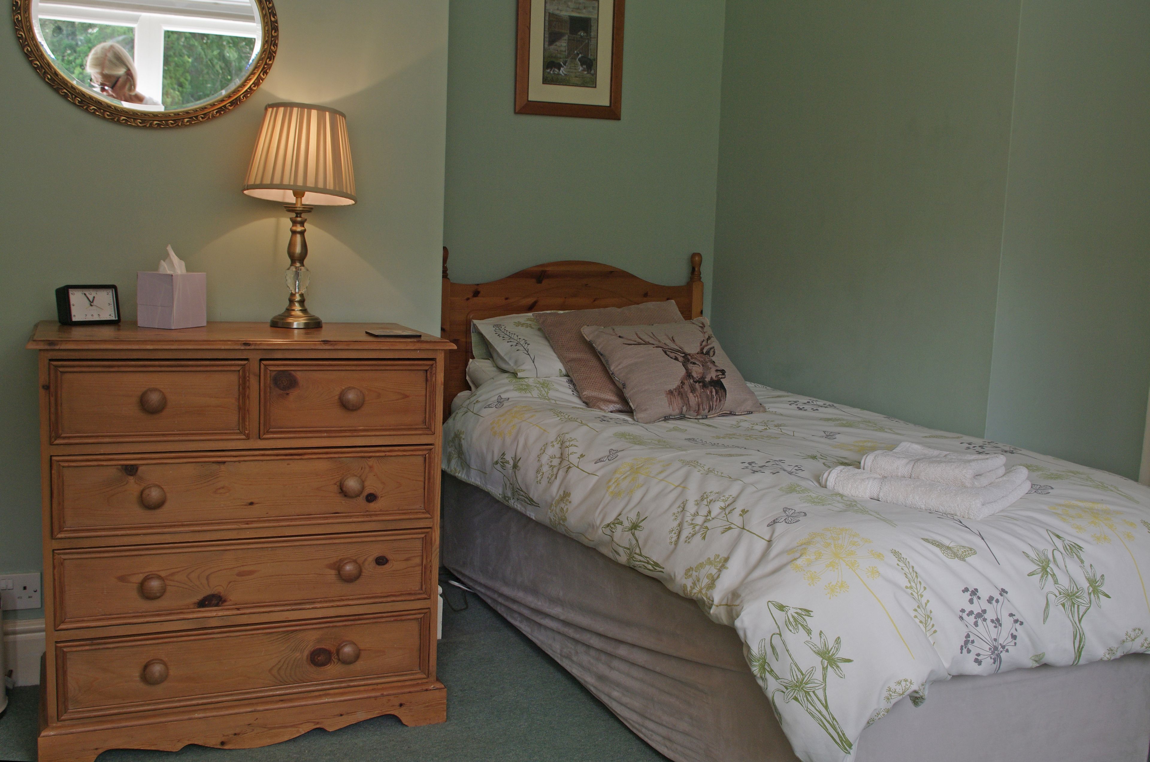 A bedroom with a wooden dresser, a bed with floral bedding, a lamp, and a framed picture on the wall.