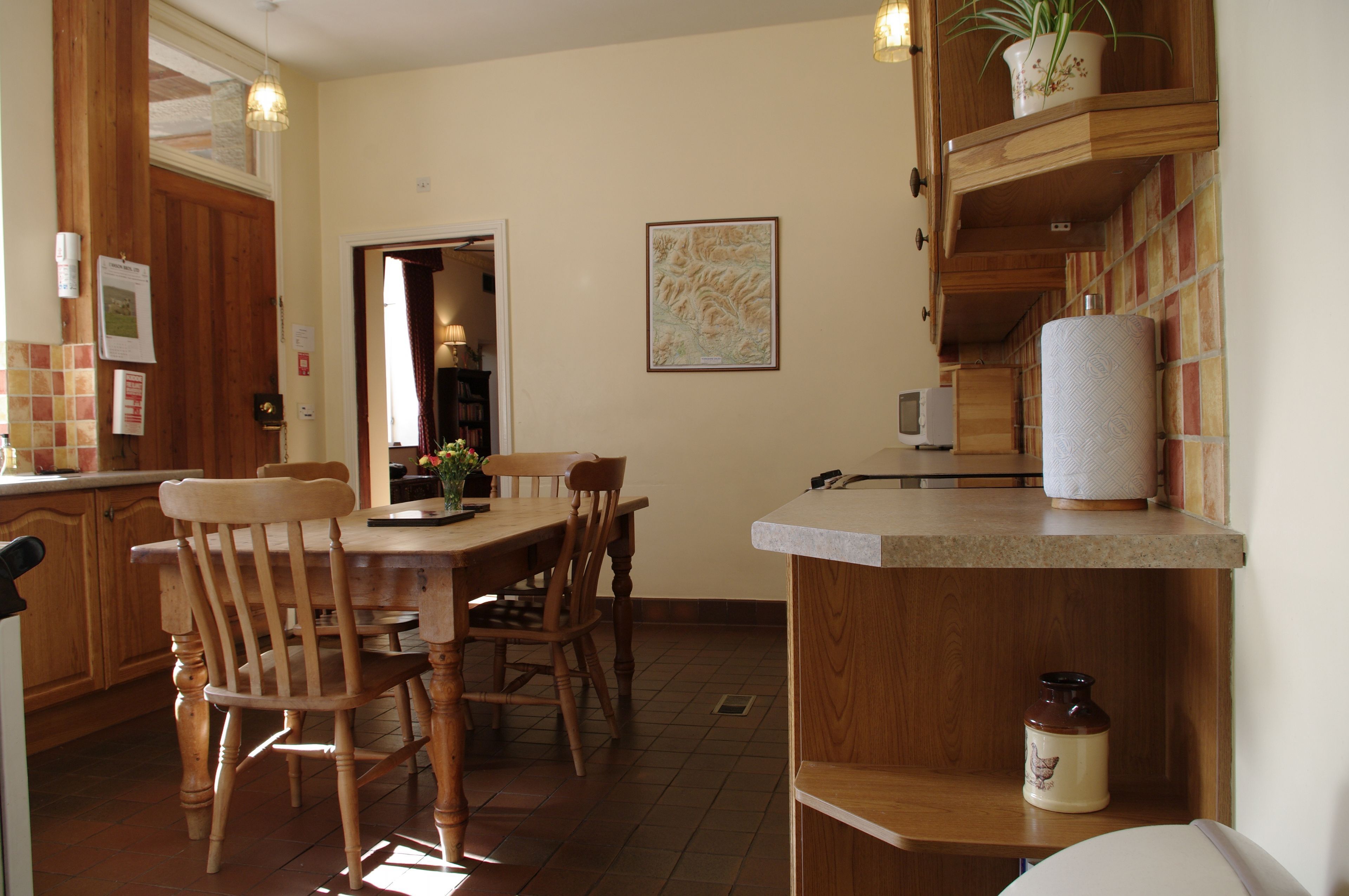 Una mesa de comedor de madera con sillas, una encimera de cocina con dispensador de toallas de papel y un mueble de madera con una planta.