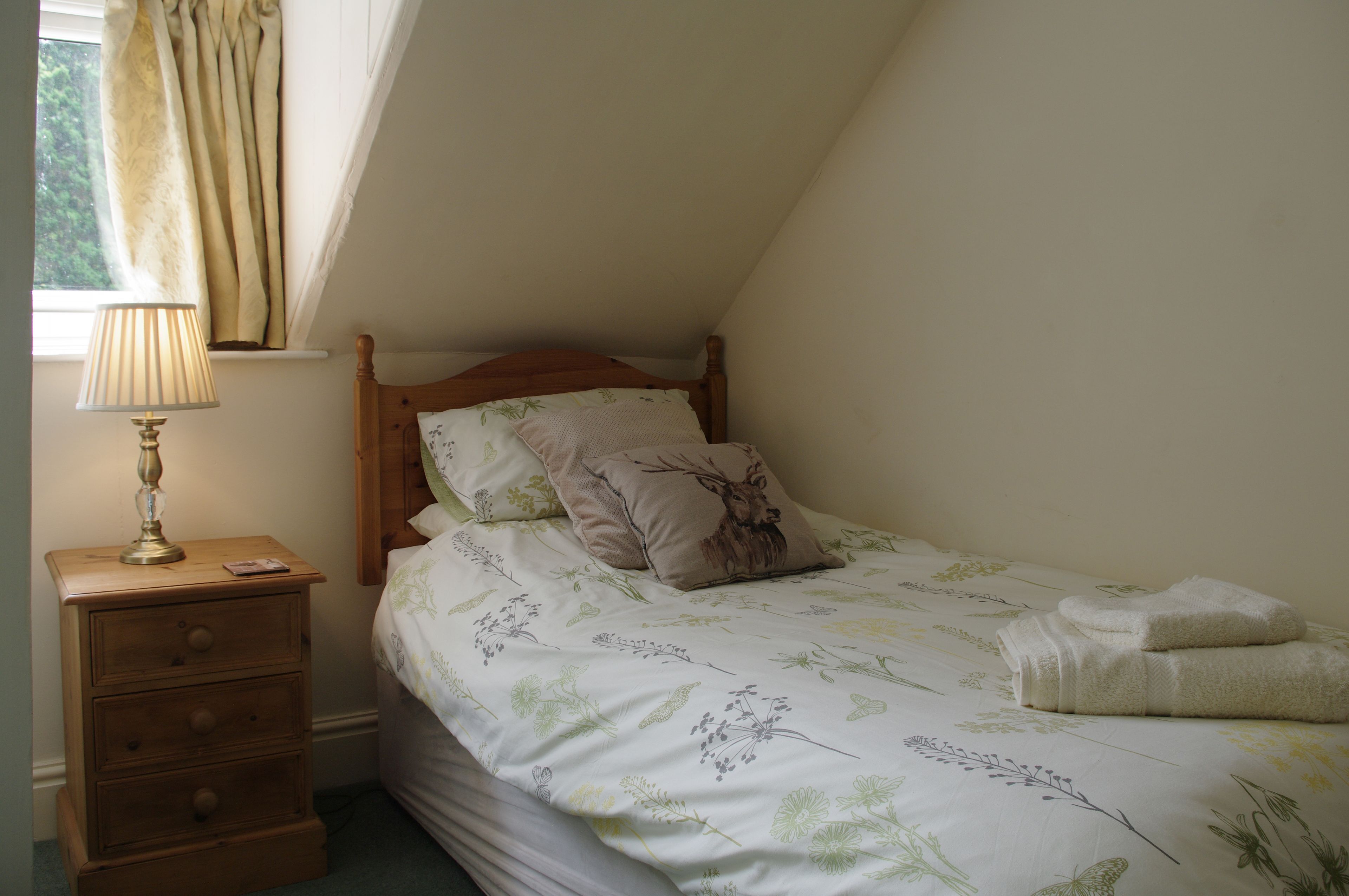 A bedroom with a bed, a nightstand, a lamp, and a window with curtains.