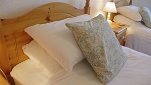 Una cama bien tendida con sábanas blancas y un cojín estampado con motivos florales, cabecera de madera y una mesita de noche con lámpara.