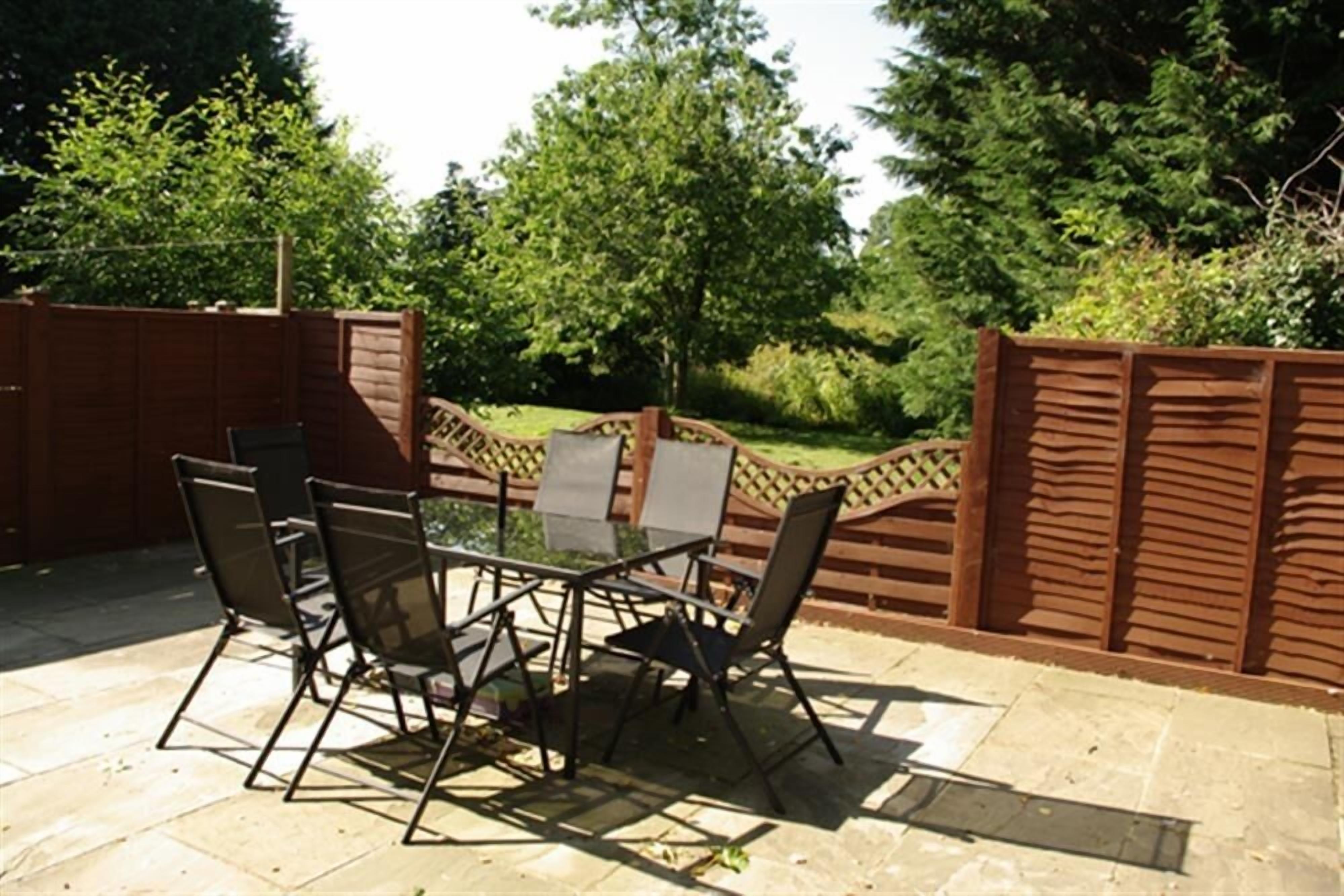 Een terras met een tafel en stoelen, omringd door een houten hek en groen.