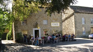 Un bâtiment en pierre avec une enseigne indiquant la présence d’un café, des tables à l’extérieur et une voiture garée.