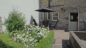 A stone building with a patio area featuring a table and chairs, surrounded by white flowers and greenery.