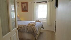 A bedroom with a bed, a window with curtains, a wall-mounted picture, and a door with frosted glass.