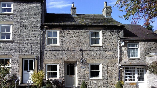 A stone building with multiple windows and a door, featuring a cobblestone pathway and small plants in front.
