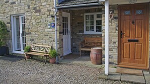 A stone building with a wooden door, a bench, and a potted plant outside.