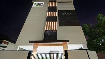 A modern hotel entrance with a vertical light feature, a sign for 'Treebo Trend Hotel Raga', and a 'HOTEL RAGA' sign.